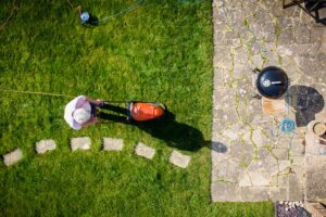 Aerial topdown view, taken by drone, depicting one man mowing his lawn with a lawnmower in his garden.