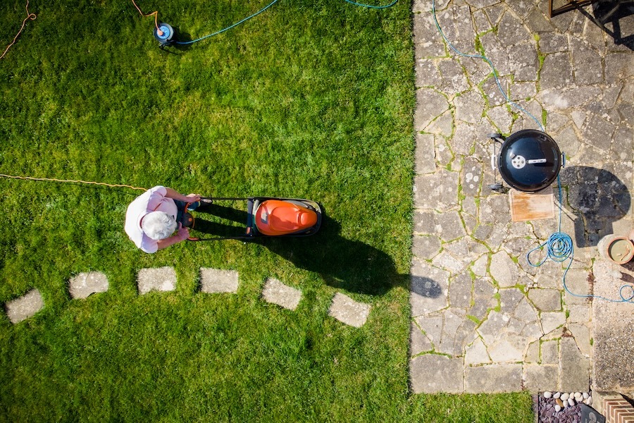 Aerial topdown view, taken by drone, depicting one man mowing his lawn with a lawnmower in his garden.